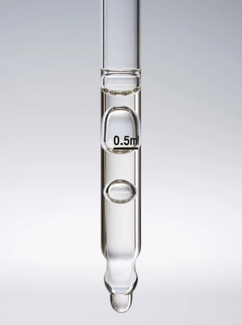 Close-up studio shot of clear glass pipette filled with liquid against a gradient gray background, displaying a liquid droplet.