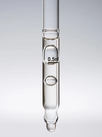 Close-up studio shot of clear glass pipette filled with liquid against a gradient gray background, displaying a liquid droplet.