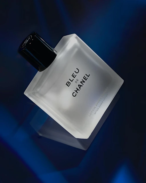 Close-up studio shot of a frosted BLEU DE CHANEL aftershave bottle against a dark blue background with diffused lighting.