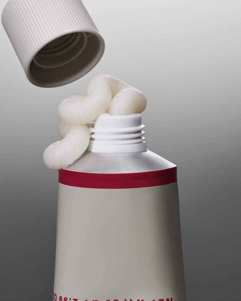 Open tube of white cream with white cap in a neutral grey studio. Focus on texture and product application, product for beauty.