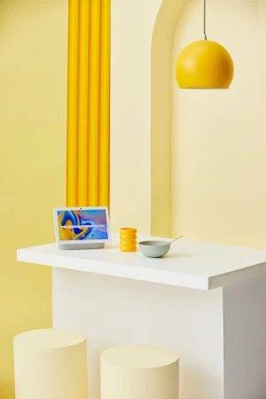 Minimalist studio shot features a laptop on a white counter, complemented by a bowl, decorative yellow objects, and a hanging pendant lamp.