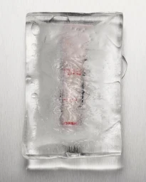 Pink cosmetic tube encased inside a melting block of ice on a brushed silver metallic surface