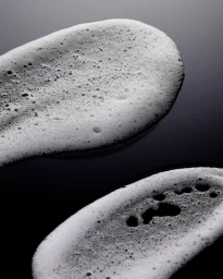 Macro shot of two textured white soap suds smears on a dark reflective surface