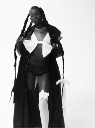 Black woman with long braided hair wearing a dark coat and white bow top styled by Sarah Starkey