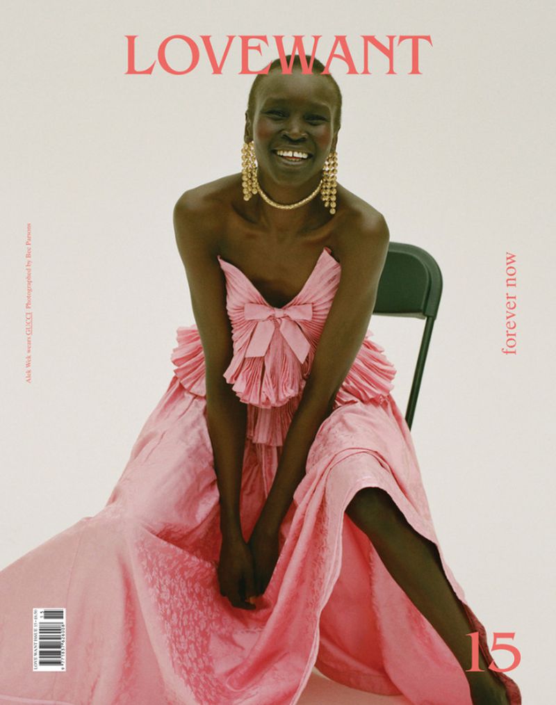 Smiling Black woman in a pink dress, gold jewelry, and bare shoulders posing on a magazine cover with light background in a studio.