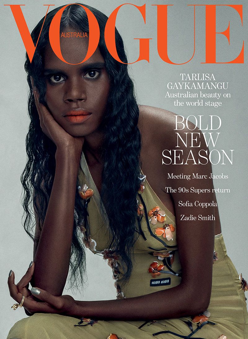 Vogue Australia cover featuring a woman with dark hair and olive green dress adorned with flower accents in a studio setting.