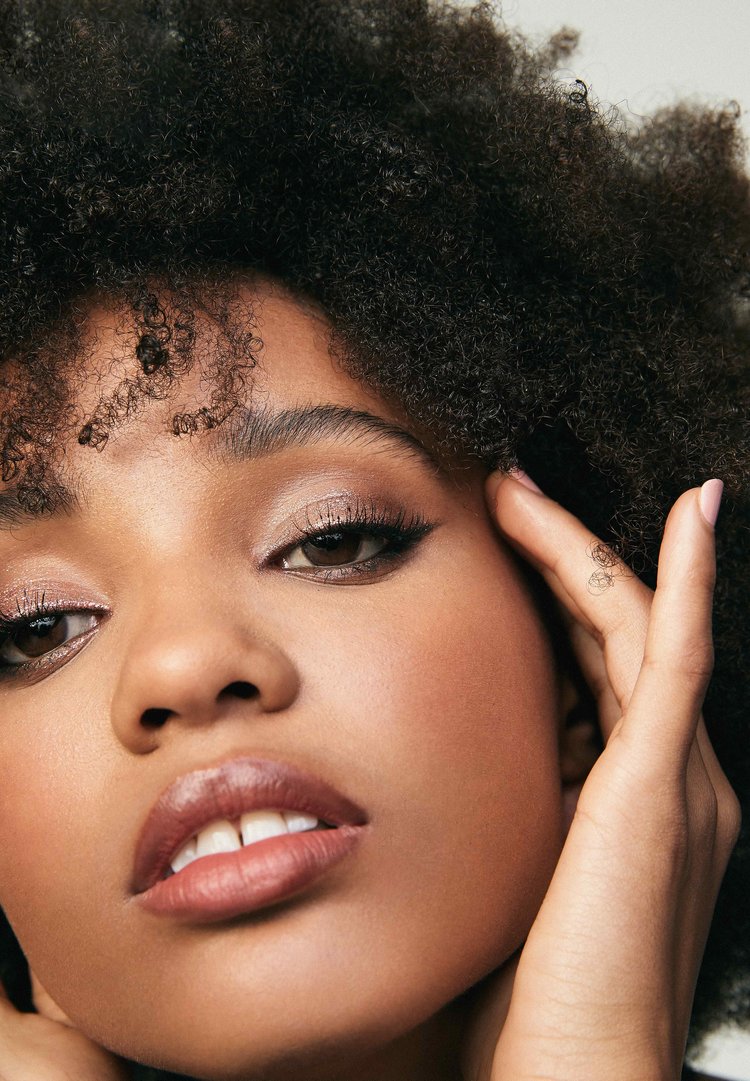 Close-up of an adult female with afro hairstyle, with mocha skin tone, posing indoors with her hands near her face.