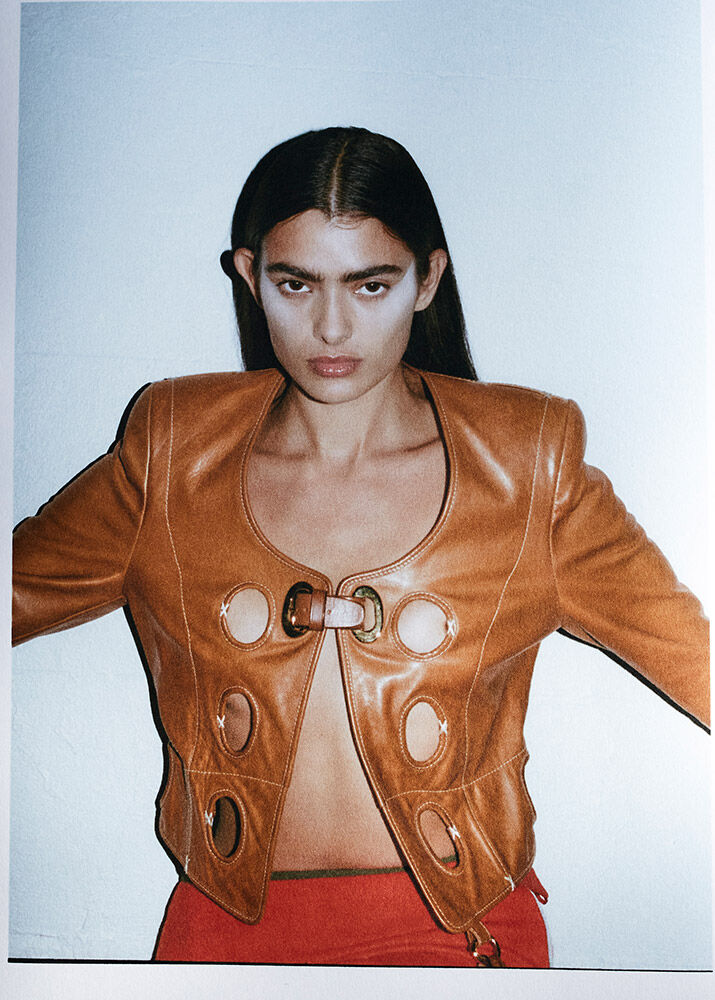 Fashion shot of a woman in a leather jacket and red skirt against a light-blue backdrop, showcasing editorial style and modern design.