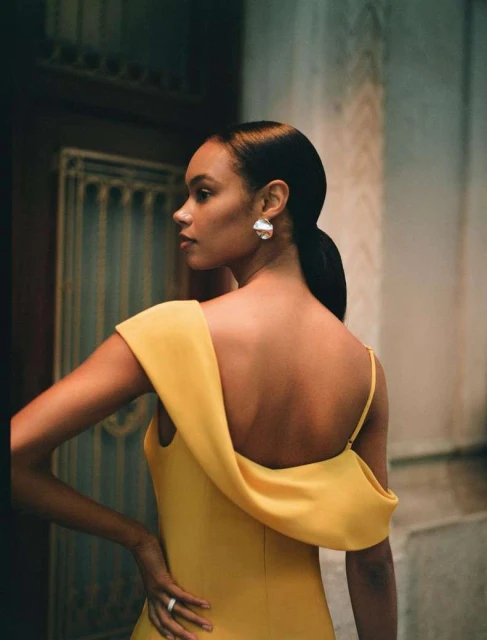 Elegant woman in yellow dress poses in architectural setting, showcasing high fashion style and sophistication, enhanced by natural lighting.