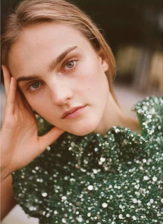 Close-up portrait of a woman wearing a green sequin top with her hand gently touching her face.