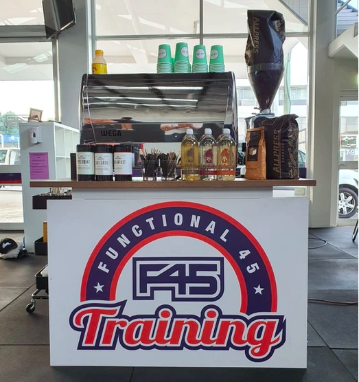 Photo of an F45 gym advertisement promoting functional fitness with an espresso machine and coffee stand displayed in the foreground.