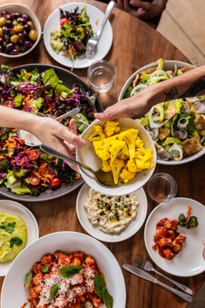 Overhead shot of a wooden table laden with a variety of vibrant dishes including colorful salads, gnocchi, cauliflower, and dips.