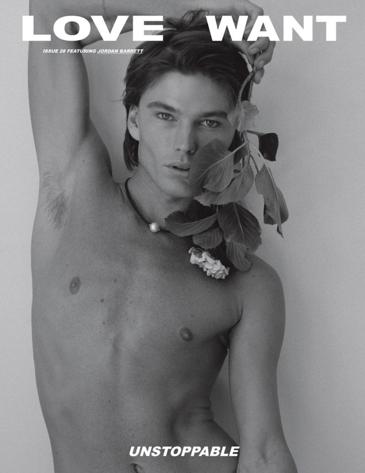 Black and white studio portrait of a shirtless male model holding a flowering branch, showcasing fashion and beauty in editorial style.