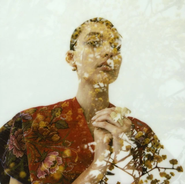 Close-up portrait of a woman with floral overlay wearing a red floral robe, against a white backdrop with translucent floral elements.