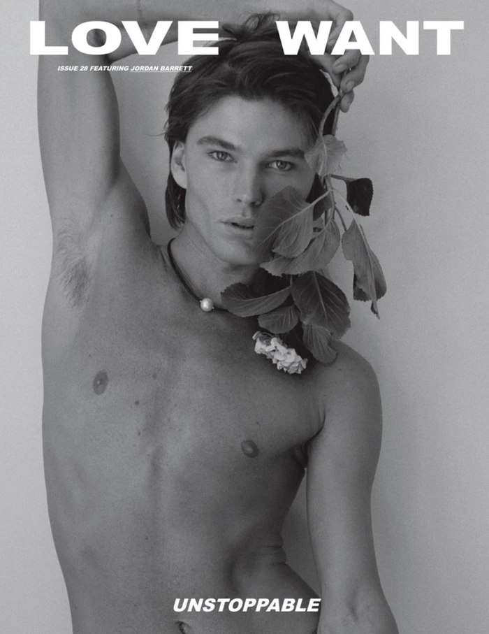 Portrait of Jordan Barrett holding leafy stems with a pearl necklace against a plain background