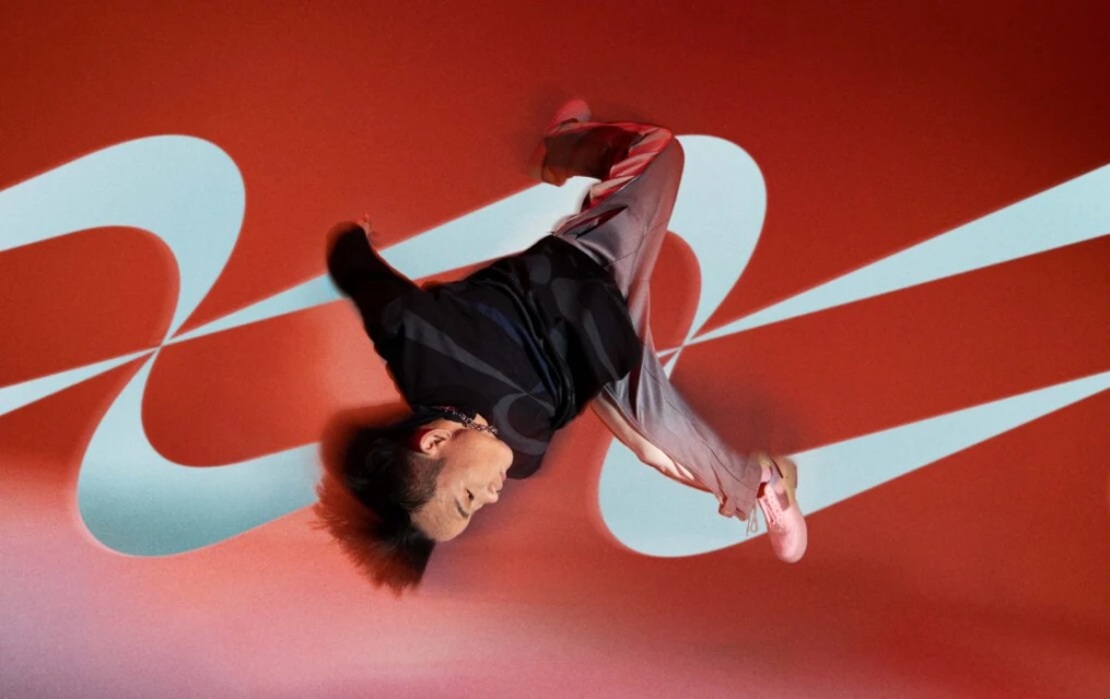 Athletic adult performs a dynamic breakdance move on a red backdrop with blue geometric designs, showcasing fitness and creative expression.