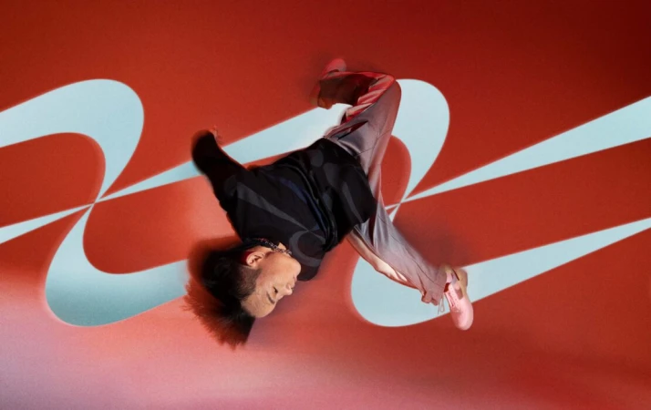 Athletic adult performs a dynamic breakdance move on a red backdrop with blue geometric designs, showcasing fitness and creative expression.
