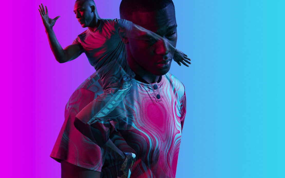Double exposure image of a Black man wearing a patterned shirt against a blue and pink gradient background, raising a hand.