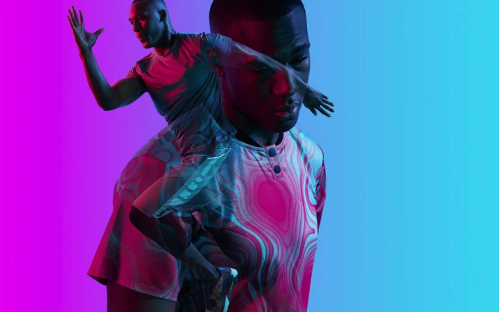 Double exposure image of a Black man wearing a patterned shirt against a blue and pink gradient background, raising a hand.