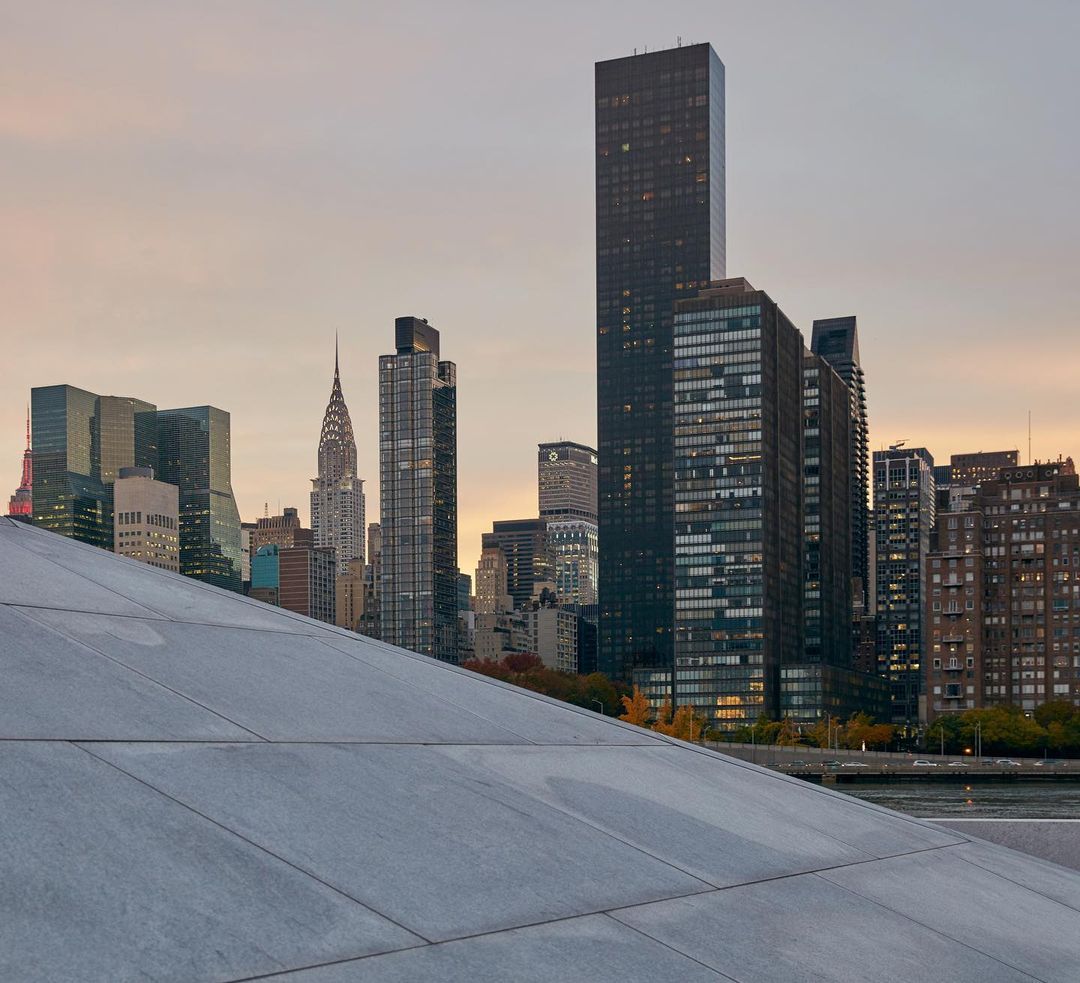 New York City skyline featuring the Chrysler Building and modern skyscrapers, viewed from a concrete structure at dusk.