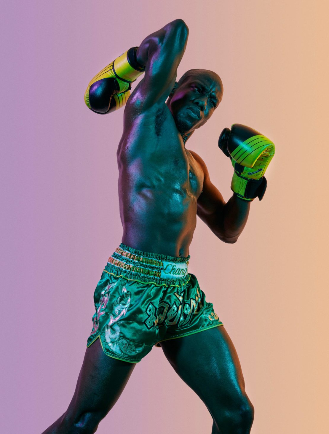 Muscular man in boxing stance with gloves and shorts in studio lighting, capturing a dynamic, athletic moment with vibrant colors.