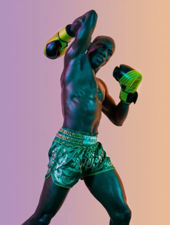 Muscular man in boxing stance with gloves and shorts in studio lighting, capturing a dynamic, athletic moment with vibrant colors.