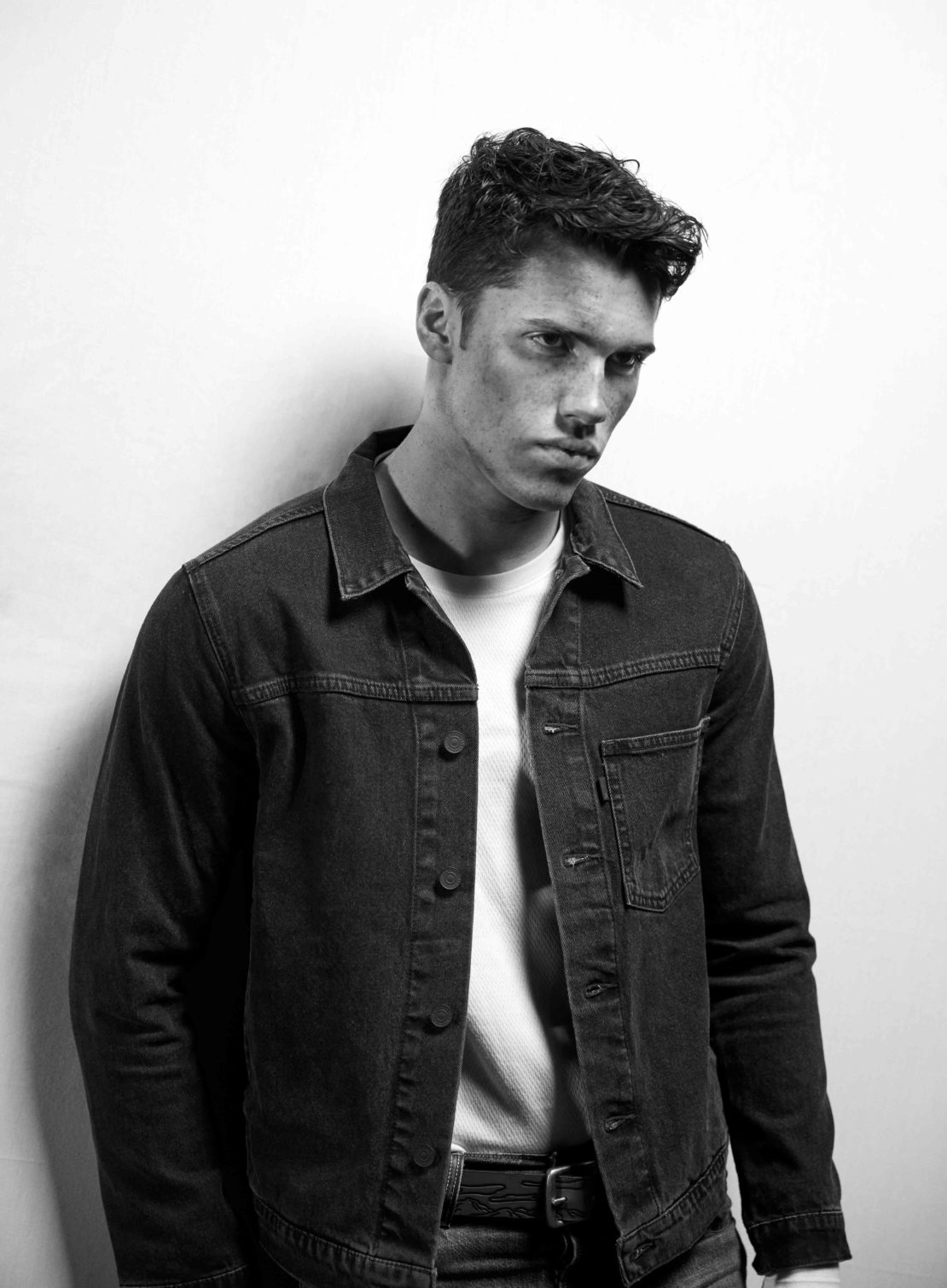 Monochrome portrait of a young man wearing a denim jacket over a t-shirt against a plain white background
