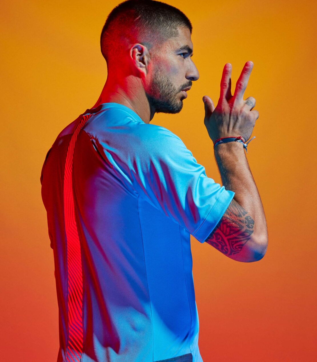 Profile portrait of a man wearing a light blue athletic jersey posing against a vibrant orange and red studio backdrop.