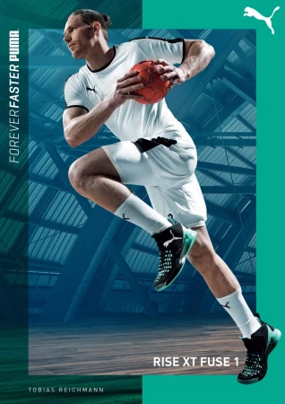 Male handball player in mid-air with ball wearing white uniform and black sneakers on court with teal and blue structural background.