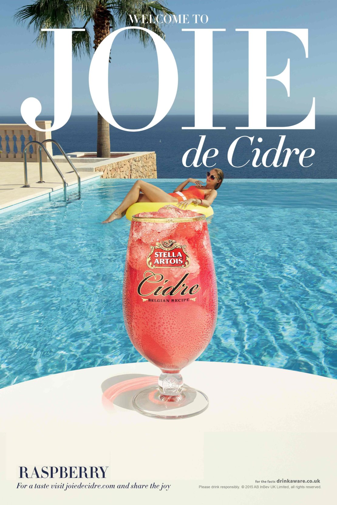Beverage ad with a cocktail glass in front of a pool and an adult female in a pool float with ocean and sky background.