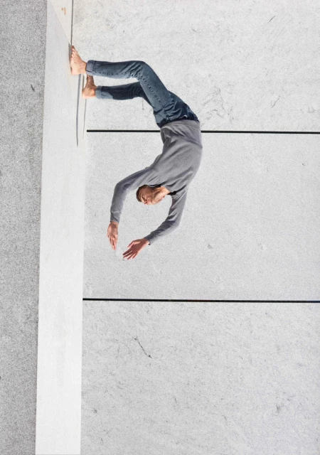 Aerial view of a flexible adult male performing a backbend against a minimalist concrete backdrop, showcasing strength and balance.