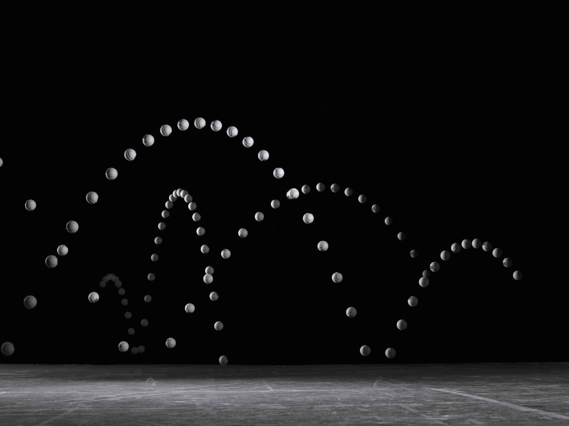 Sequential motion capture of a tennis ball bouncing repeatedly against a dark background, illustrating its parabolic trajectory.