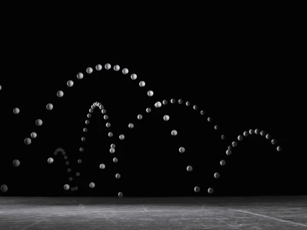 Sequential motion capture of a tennis ball bouncing repeatedly against a dark background, illustrating its parabolic trajectory.
