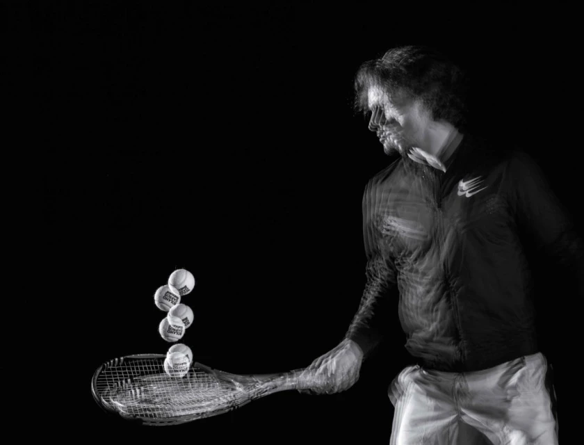 Action shot of a male athlete hitting tennis balls with a racket on a black background. Motion blur shows the speed and movement.