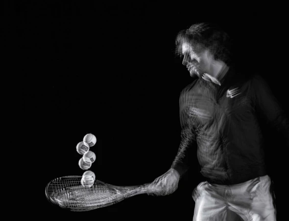 Action shot of a male athlete hitting tennis balls with a racket on a black background. Motion blur shows the speed and movement.
