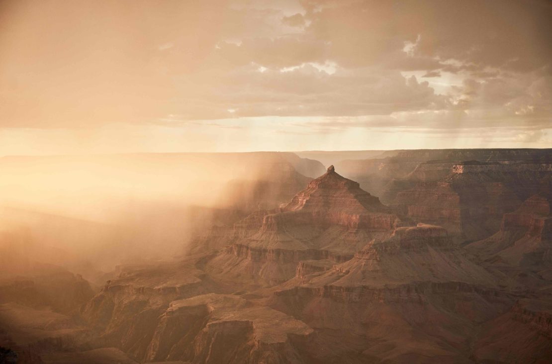 Grand Canyon landscape featuring layered rock formations and sunlight filtering through the clouds, creating depth and dramatic lighting.