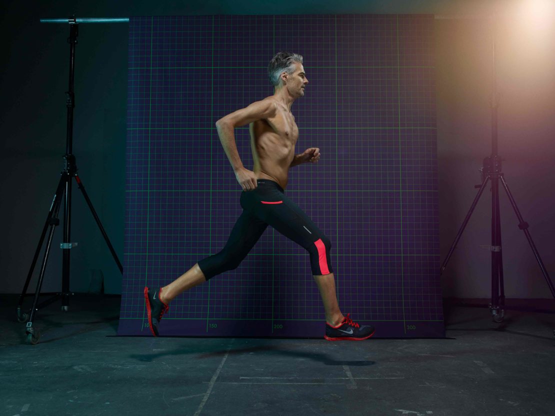 Man running in place with athletic apparel in a studio setting with two light stands on either side, against a purple grid backdrop.