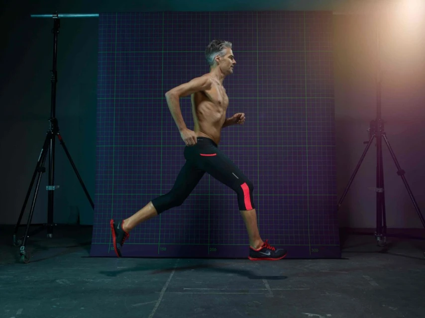 Man running in place with athletic apparel in a studio setting with two light stands on either side, against a purple grid backdrop.
