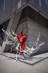Dancer in red clothing mid-air with white fluid splashes against a concrete building exterior
