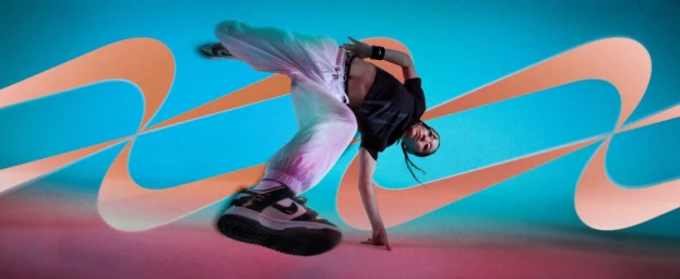 Dancer in motion wearing a black crop top and white track pants against a vibrant blue and pink wavy patterned background.
