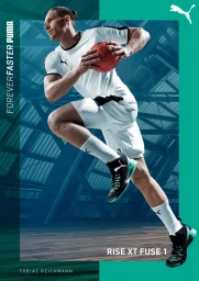 Man wearing white athletic jersey and shorts running while holding a red handball inside a large gymnasium