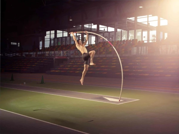 Male pole vaulter suspended in mid-air holding a flexible pole inside a large indoor stadium arena.
