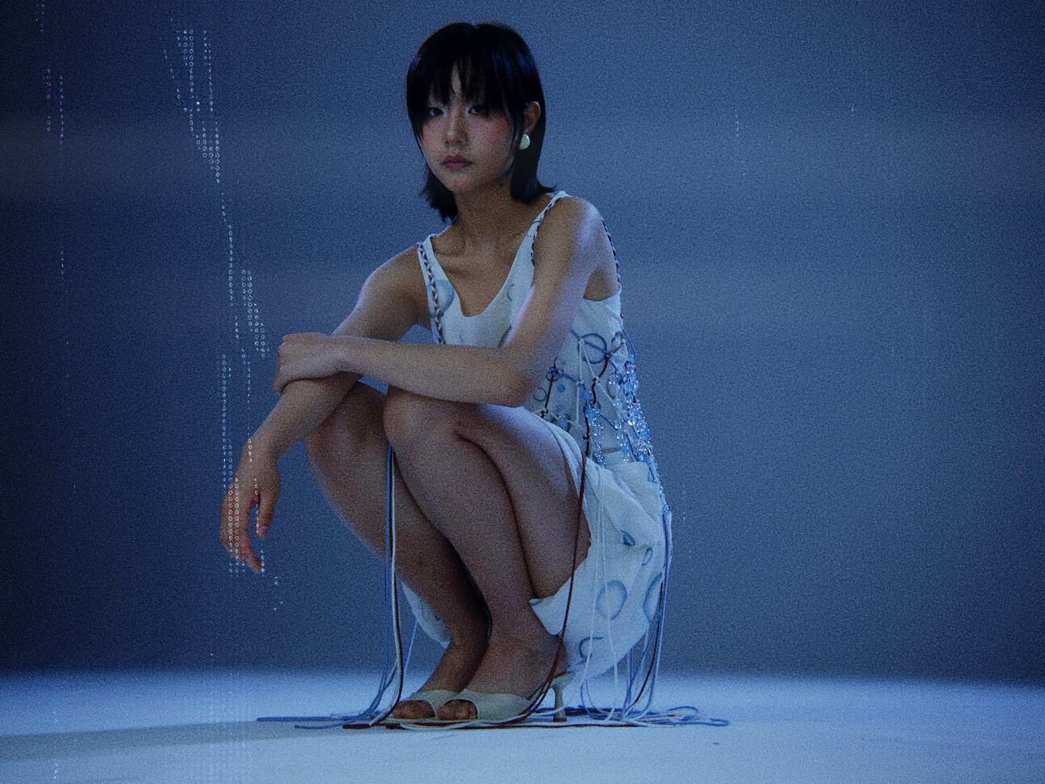 An Asian woman with short black hair is crouching and wearing a white dress with blue accents, posing in a photo studio with blue background.