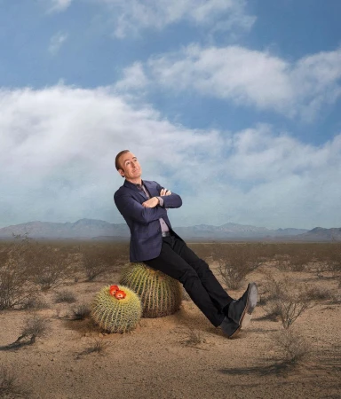 Bob Odenkirk leaning back with arms crossed while sitting on a round cactus in a desert landscape