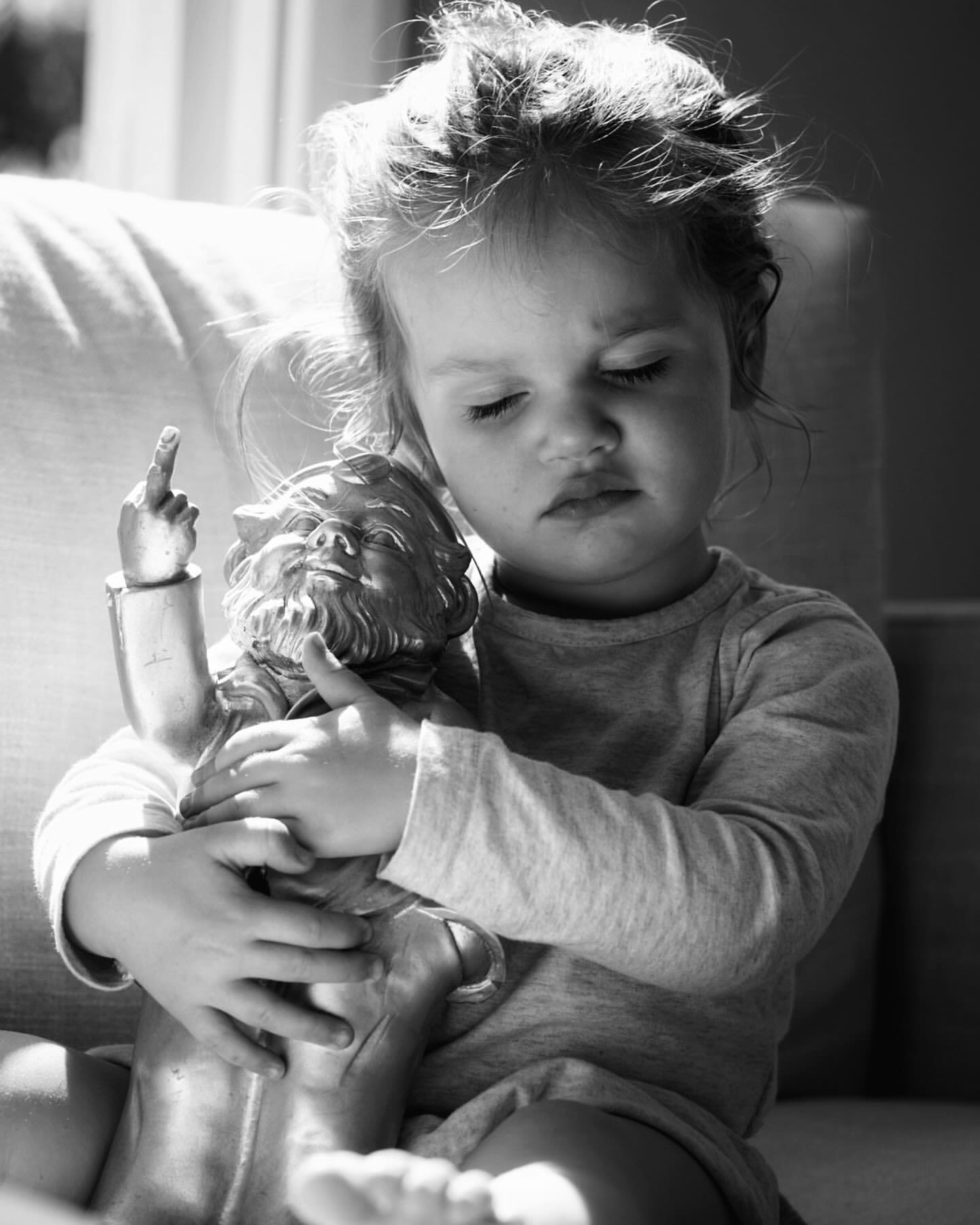 Black and white shot of a toddler holding a figurine indoors with soft natural light, creating a serene and intimate portrait.