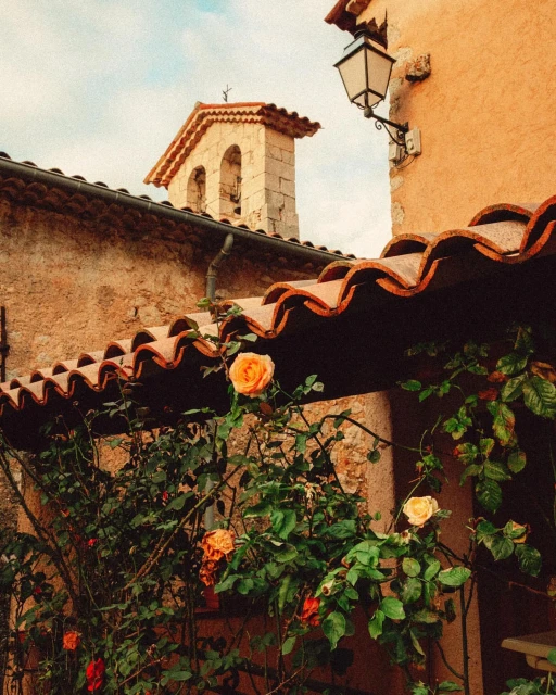 Exterior view of a charming old building with a stone bell tower, a lamp post, and climbing roses with yellow and orange flowers.