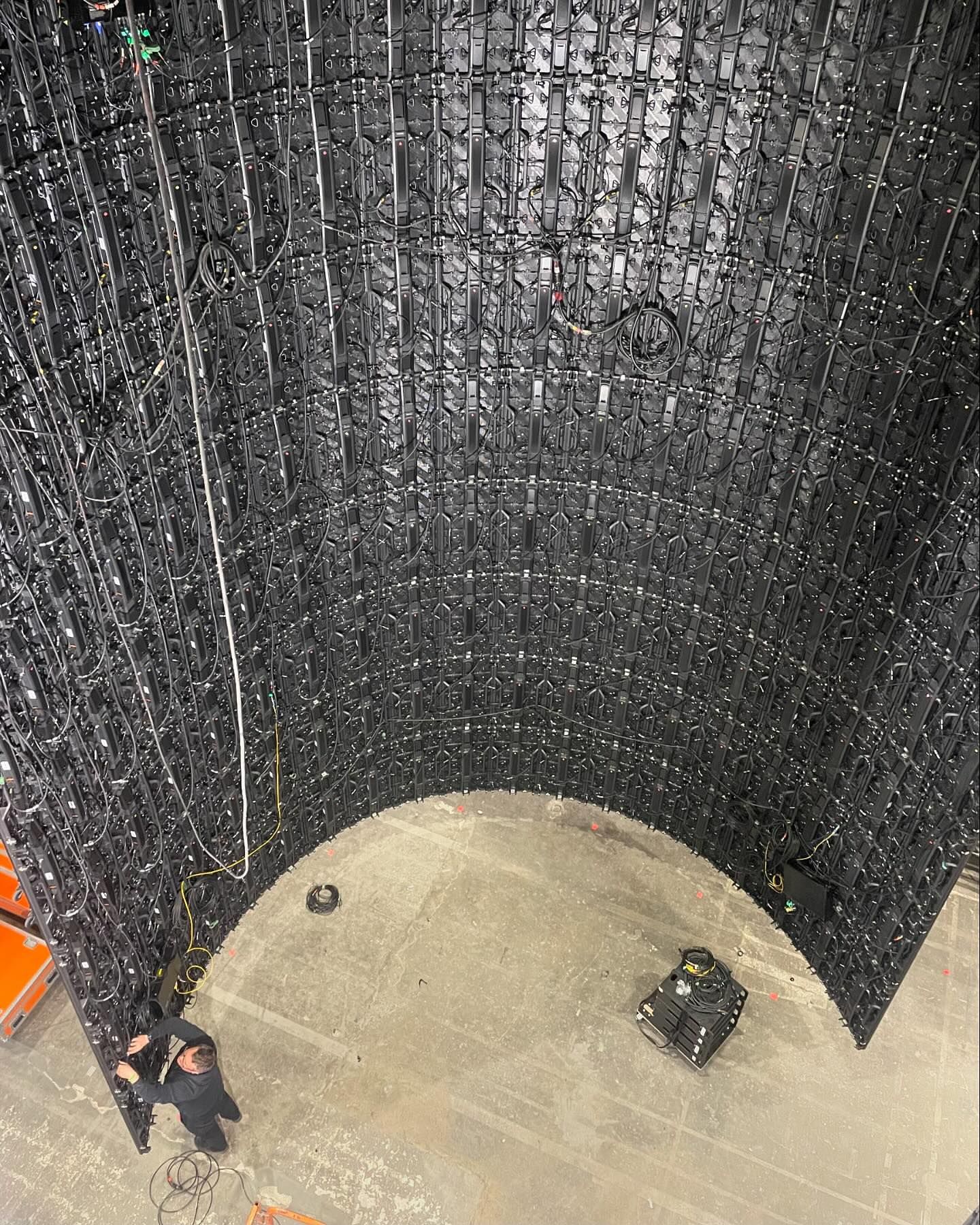 A panoramic shot inside a curved wall structure built of interconnected black panels, with a maintenance worker and equipment inside.