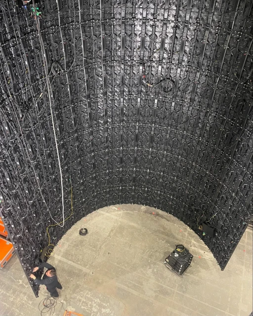 A panoramic shot inside a curved wall structure built of interconnected black panels, with a maintenance worker and equipment inside.