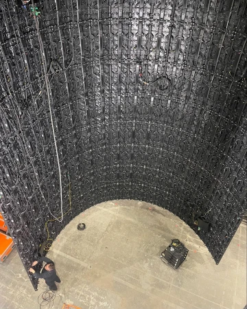 A panoramic shot inside a curved wall structure built of interconnected black panels, with a maintenance worker and equipment inside.
