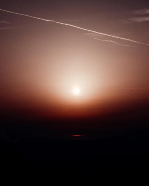 Sunset over a dark horizon with a visible contrail. The light creates a warm glow and highlights the atmospheric perspective.